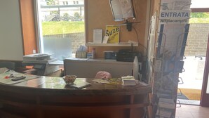 A reception desk with a computer monitor, a bulletin board, and a window with a view of buildings and greenery.