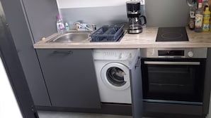 Ett kompakt kök med tvättmaskin, ugn och kaffebryggare på bänkskivan.