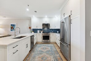 A modern kitchen with white cabinets, stainless steel appliances, and a blue patterned rug. - Beautiful Spacious Oceanfront Condo On Isle of Palms (Isle of Palms)