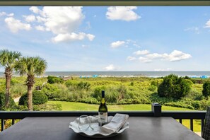 A balcony with a table, a bottle of wine, and glasses on a tray, overlooking a coastal landscape with greenery and the sea. - Beautiful Spacious Oceanfront Condo On Isle of Palms (Isle of Palms)