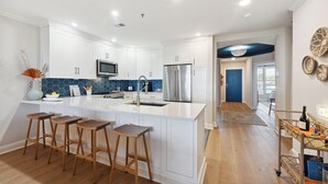 A modern kitchen with white cabinets, a stainless steel refrigerator, and a large island with bar stools. - Beautiful Spacious Oceanfront Condo On Isle of Palms (Isle of Palms)