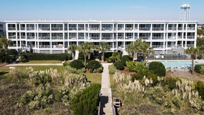 A multi-story hotel with balconies, a swimming pool, and a water tower in the background. - Beautiful Spacious Oceanfront Condo On Isle of Palms (Isle of Palms)