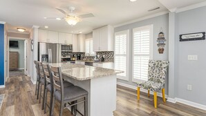 A modern kitchen with white cabinets, a granite island, and a ceiling fan. - Private Beach House, Pet Friendly, Close To Beach + Free Attraction Tickets! (North Myrtle Beach)