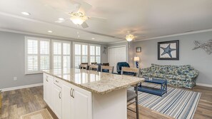 Cozinha ampla com uma ilha grande, área de jantar com cadeiras e sala de estar com sofá e decoração de estrela-do-mar.