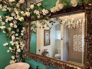 Ein Badezimmer mit einem großen, verzierten Spiegel, einer Kristallleuchter und einer grünen Wand.