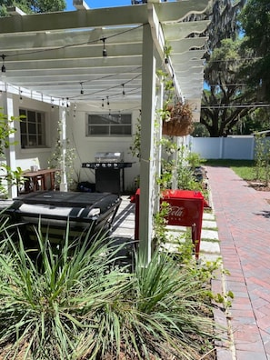 Eine Außenpatio mit Grill, einem roten Briefkasten und einer Pergola mit Lichterketten.