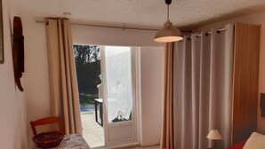 A room with a bed, a table with a chair, a window with curtains, and a hanging light fixture.