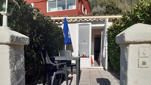 A patio with a table and chairs, a blue umbrella, and a white building with a door.