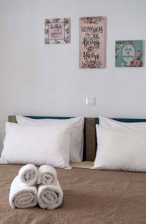 A neatly made bed with white pillows and rolled towels, a wooden headboard, and two wall decorations with floral designs and inspirational quotes.