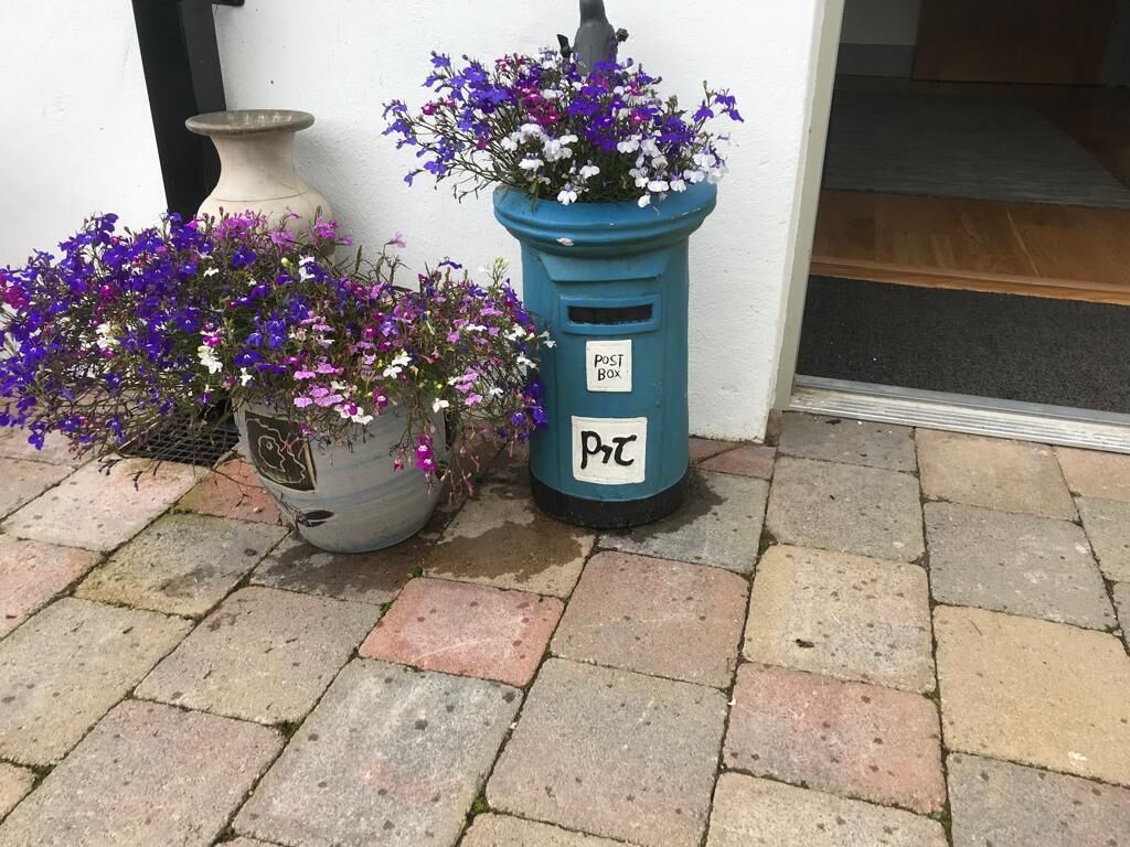 Un buzón con la etiqueta 'Post Box' y una maceta con flores moradas.