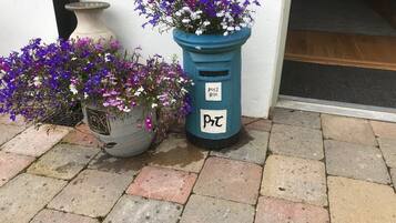 Un buzón con la etiqueta 'Post Box' y una maceta con flores moradas.