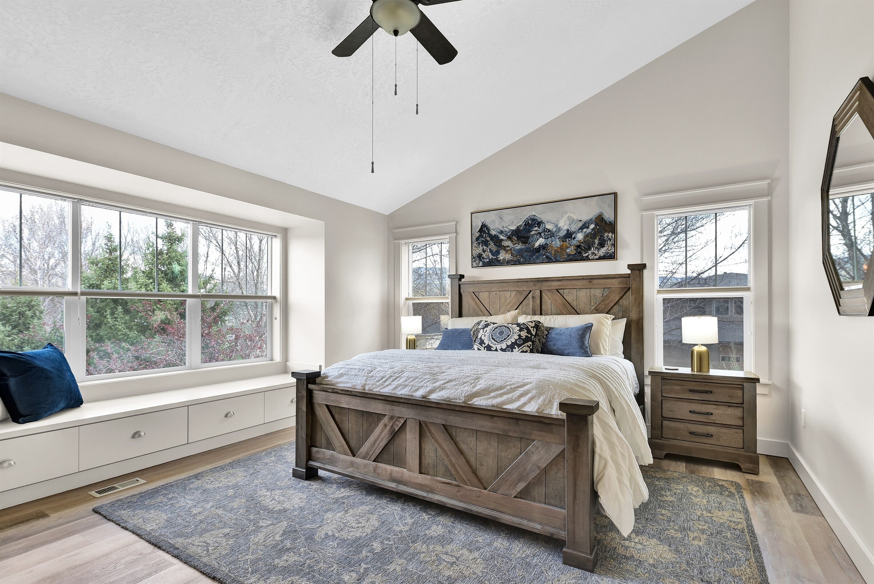 A bedroom with a wooden bed, large windows, a ceiling fan, and a painting on the wall.