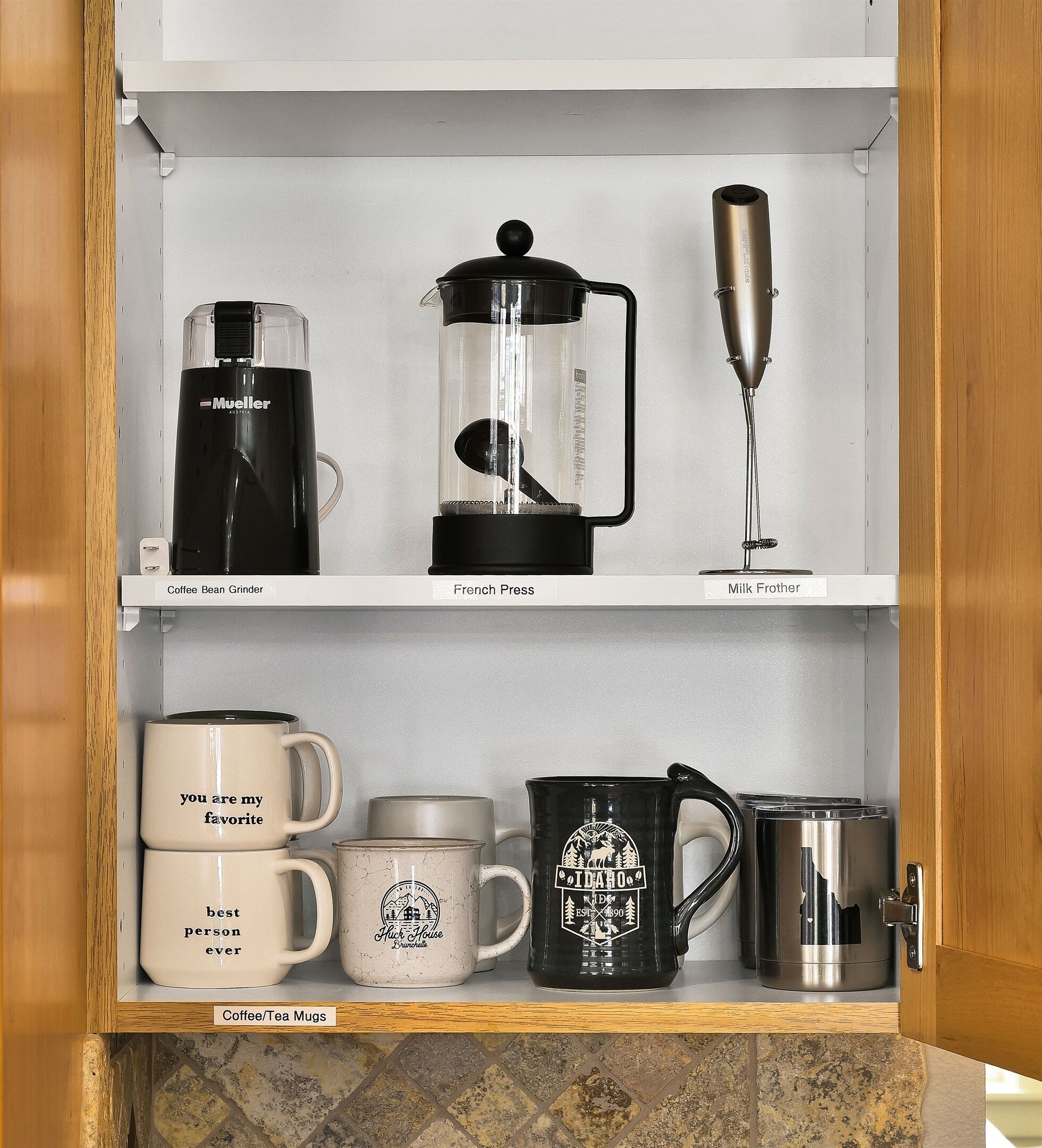 Un meuble de cuisine contenant un moulin à café, une cafetière à piston, un mousseur à lait et des tasses à café/thé.