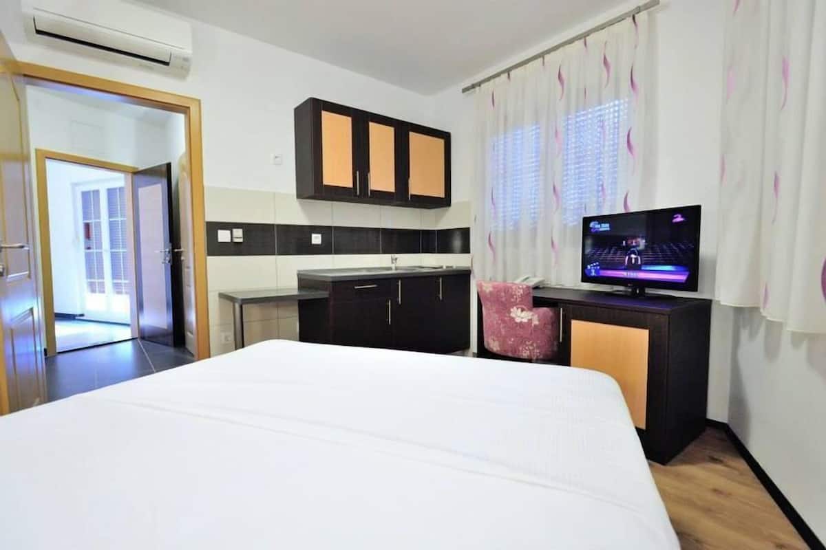 A hotel room with a bed, a TV, a small kitchenette, and a bathroom visible through an open door.