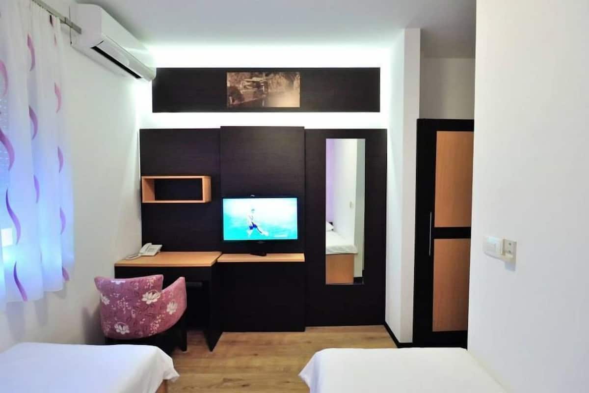 A hotel room with a bed, a desk with a TV, a phone, and a chair.