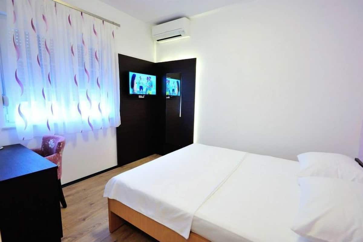 A hotel room with a bed, a desk, and two televisions mounted on the wall.