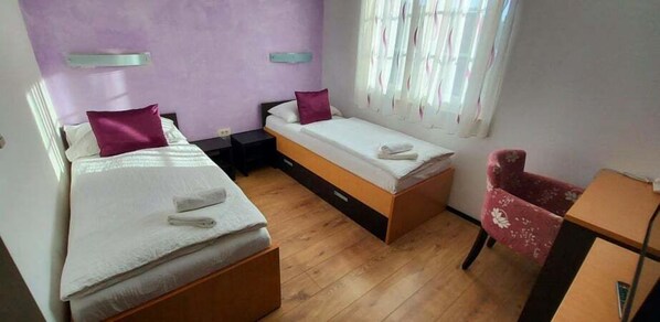 A room with two beds, a wooden floor, a desk, and a chair.