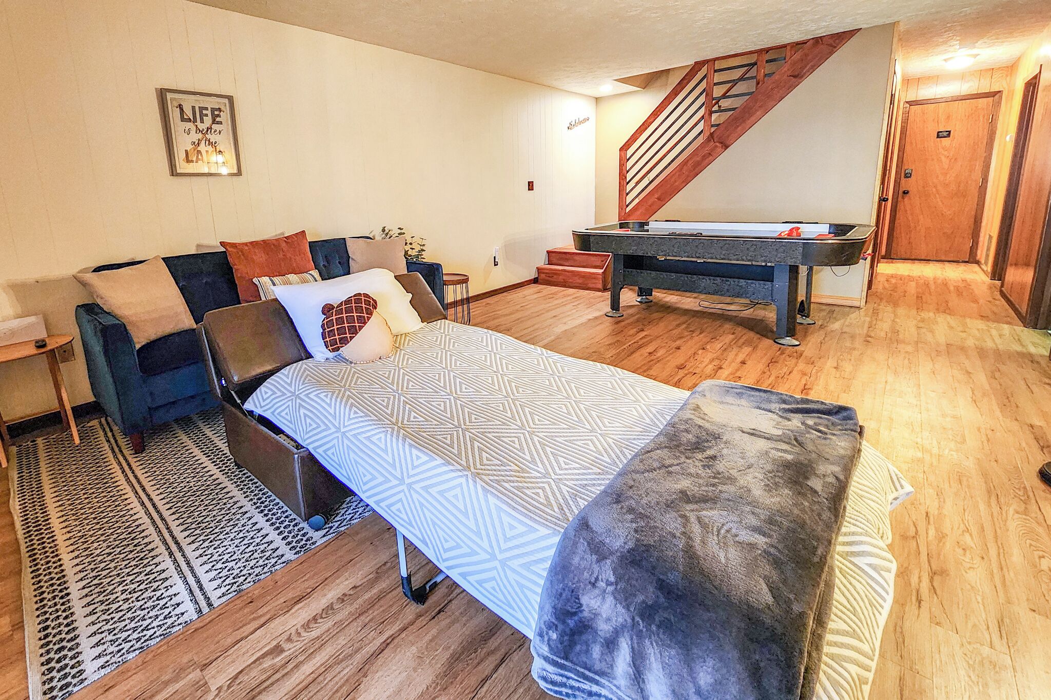 A cozy living room with a sofa, a bed, a pool table, and a staircase.
