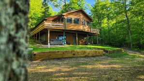 Eine zweistöckige Holzhütte mit Balkon, umgeben von einem Wald.