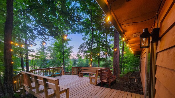 Eine Holzterrasse mit Tisch und Stühlen, umgeben von Bäumen und Lichterketten.