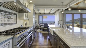 Een moderne keuken met een groot eiland, roestvrijstalen apparatuur en uitzicht op de oceaan.