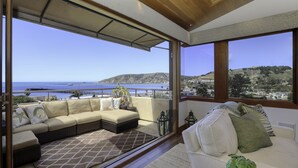 Een balkon met een bank en stoelen, met uitzicht op de zee en een steiger.