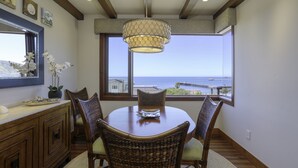Een eetgedeelte met uitzicht op de oceaan, met een houten tafel, rieten stoelen en een hanglamp.