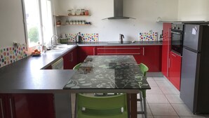 Een moderne keuken met rode kastjes, een zwart aanrecht en een groene stoel. Er is een raam dat natuurlijk licht binnenlaat en een roestvrijstalen koelkast.