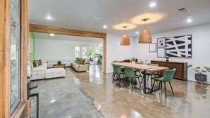 Un vaste espace de vie doté d’un grand plafond en bois, d’une table à manger avec des chaises, et d’un coin cuisine à l’arrière-plan.