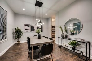 Un comedor moderno con una mesa rectangular, sillas negras y una mesa consola de vidrio con objetos decorativos.