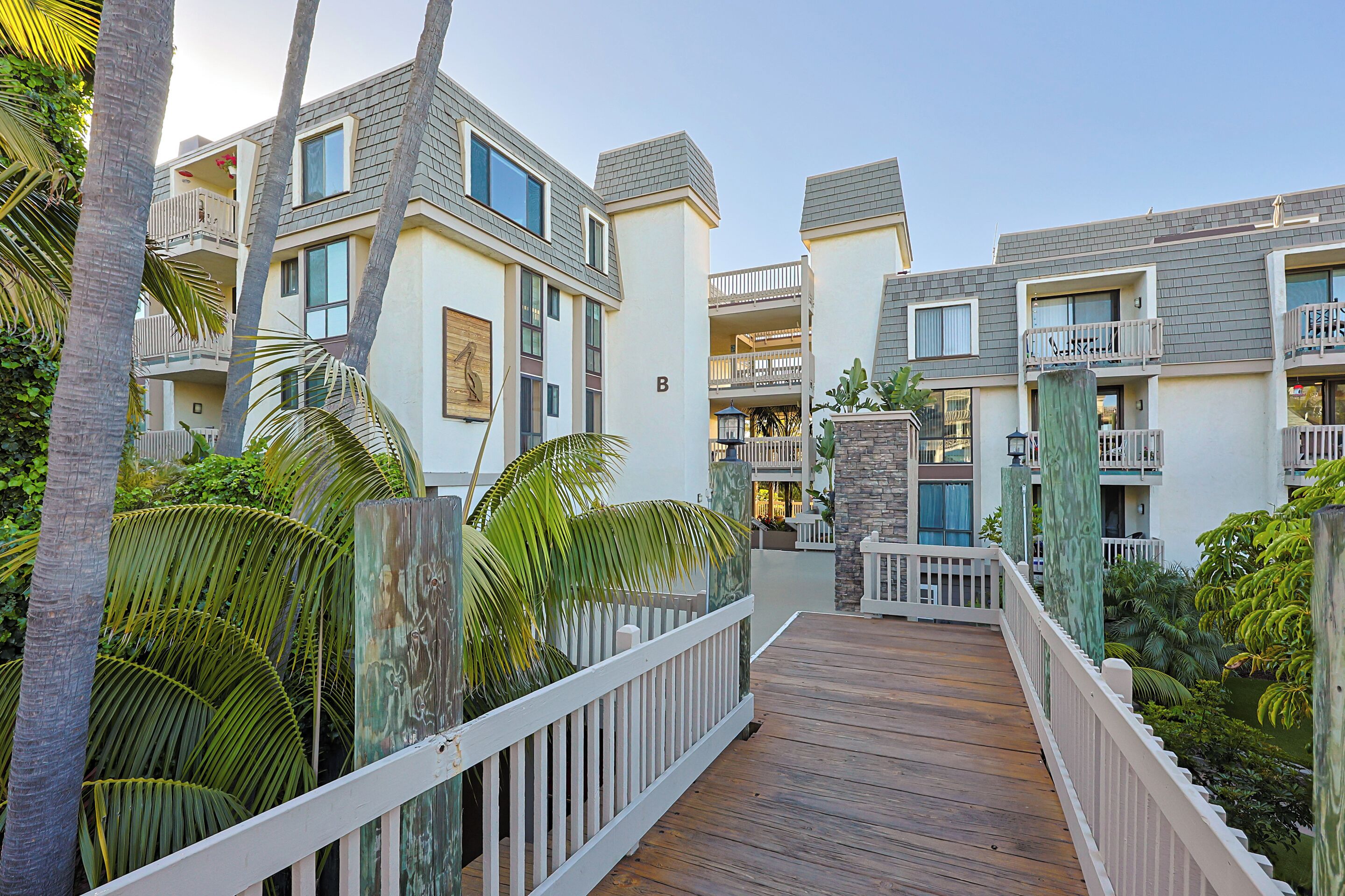 Un hotel de varios pisos con balcones, una terraza de madera y plantas tropicales.