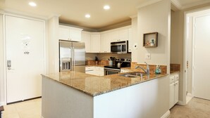 A modern kitchen with white cabinetry, granite countertops, stainless steel appliances, and recessed ceiling lighting.