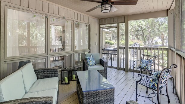 A covered porch with wicker furniture, a ceiling fan, and large windows offering views of the outdoors.