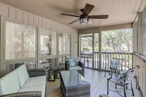 A covered porch with wicker furniture, a ceiling fan, and large windows offering views of the outdoors.