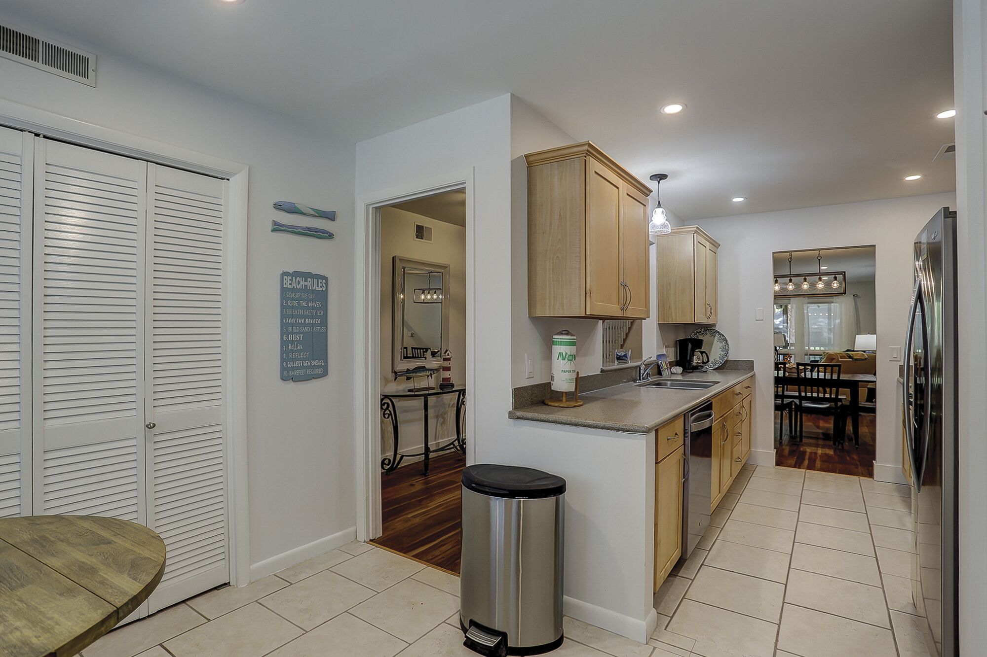 A modern kitchen with wooden cabinets, a stainless steel trash can, and a dining area with a table and chairs.