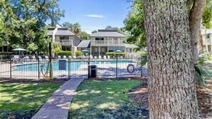 A pool area with a fenced pool, a pathway, and a building with a balcony in the background.