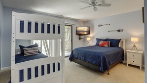 A bedroom with a bunk bed, a single bed, a ceiling fan, a TV, and decorative wall art.
