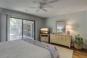 A bedroom with a bed, a TV, a dresser, a mirror, and a ceiling fan.
