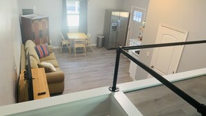 A living room with a sofa, a coffee table, and a TV stand. There is a dining area with a table and chairs. A kitchen with a refrigerator and a sink is visible. - Cheerful studio by LionsBridge, short 🚶‍♀️to downtown. (St. Augustine)
