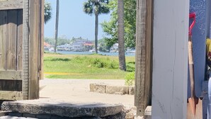 An open wooden door leading to a paved area with a view of a body of water and buildings in the distance. - Cheerful studio by LionsBridge, short 🚶‍♀️to downtown. (St. Augustine)