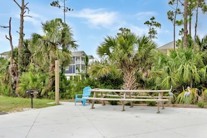 A picnic table with chairs, surrounded by palm trees and a building in the background. - A Little Extra Beachfront RV Lot ~ Lagniappe Shores RV Lot (Indian Pass)