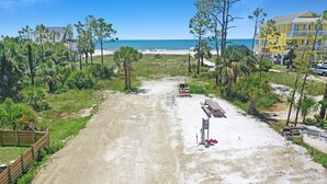 Ein Strandgrundstück mit einem Feldweg, der zu einer Holzbank und einem Picknicktisch führt, umgeben von Palmen und Blick auf das Meer.