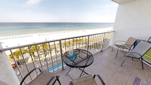 Un balcon avec vue sur la plage, une piscine et une table avec des chaises.