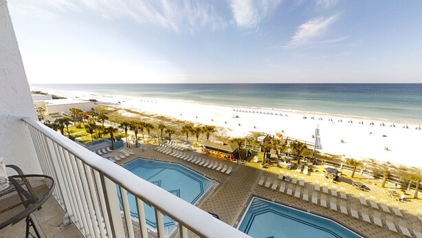Un balcon avec vue sur une plage et deux piscines.