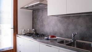 A modern kitchen with white cabinets, a stainless steel sink, and a gas stove. - Detached house in San Vito Lo Capo near the beach (San Vito Lo Capo)