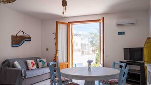 A room with a grey sofa, blue chairs, a round table, a TV, and an air conditioning unit. - Detached house in San Vito Lo Capo near the beach (San Vito Lo Capo)