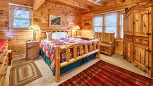 A wooden cabin bedroom with a bed, two bedside tables, a nightstand, a wardrobe, a ceiling fan, and two windows with blinds. - 3 Bedroom, Beautiful Mountain Views, Wireless Internet, Located behind MVCC (MAGGIE VALLEY)