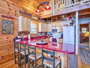A wooden cabin kitchen with a red countertop, wooden cabinets, a microwave, a stove, and a refrigerator. - 3 Bedroom, Beautiful Mountain Views, Wireless Internet, Located behind MVCC (MAGGIE VALLEY)