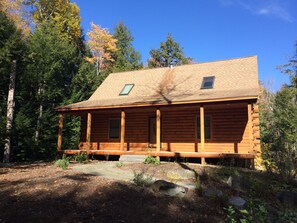 Eine Blockhütte mit Veranda, umgeben von Bäumen und blauem Himmel.