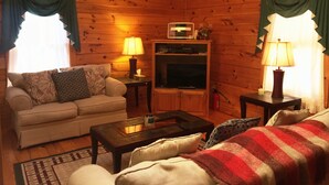 Un acogedor interior de cabaña de madera con un sofá, una mesa de centro, un televisor y lámparas.